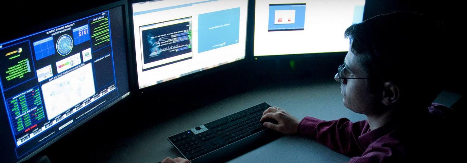 Student seated at a bank of three computer screens